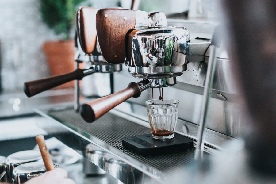 A commercial coffee machine pouring an espresso shot into a small glass
